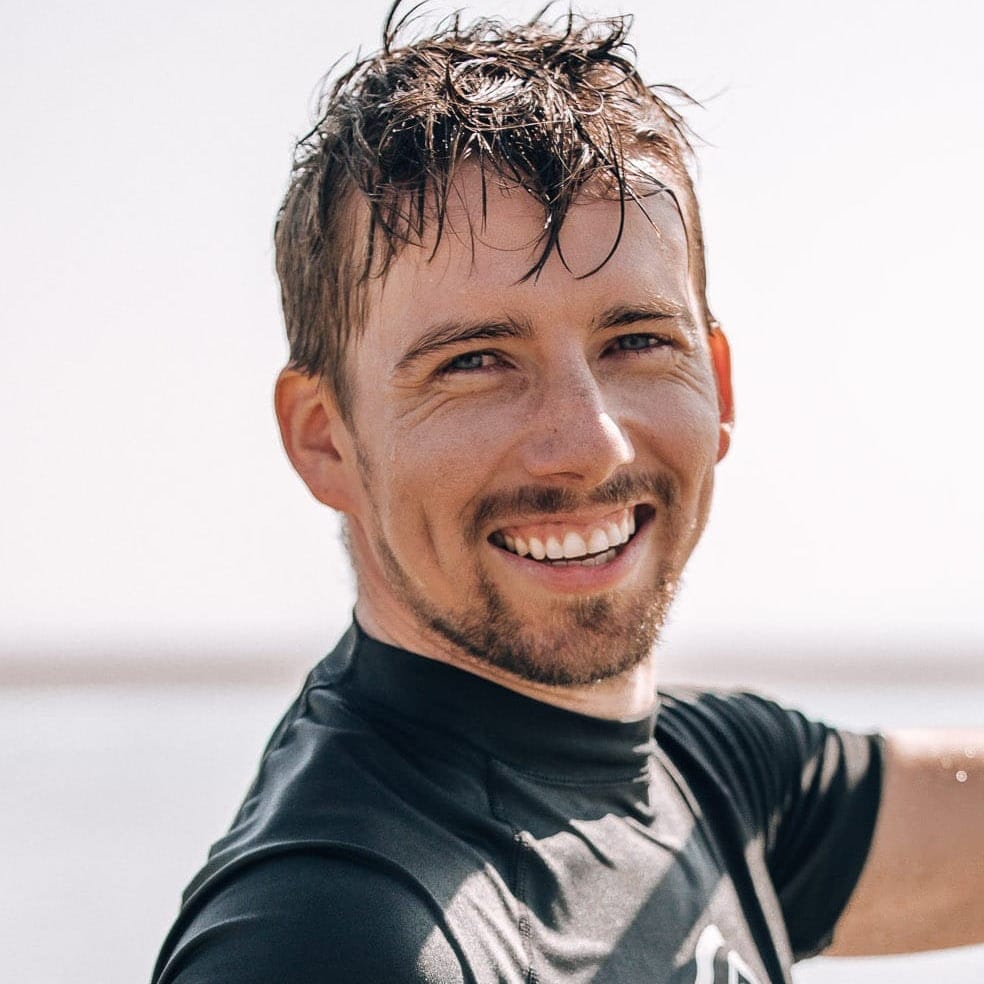 A picture of me wearing a rash guard and wet hair on a sunny day smiling at the camera.